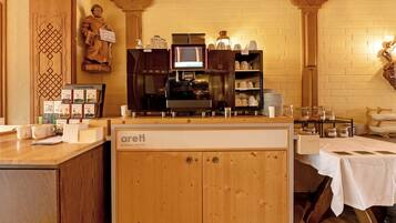 Un interior de cafetería con mostrador de madera, una máquina de café y una estatua.