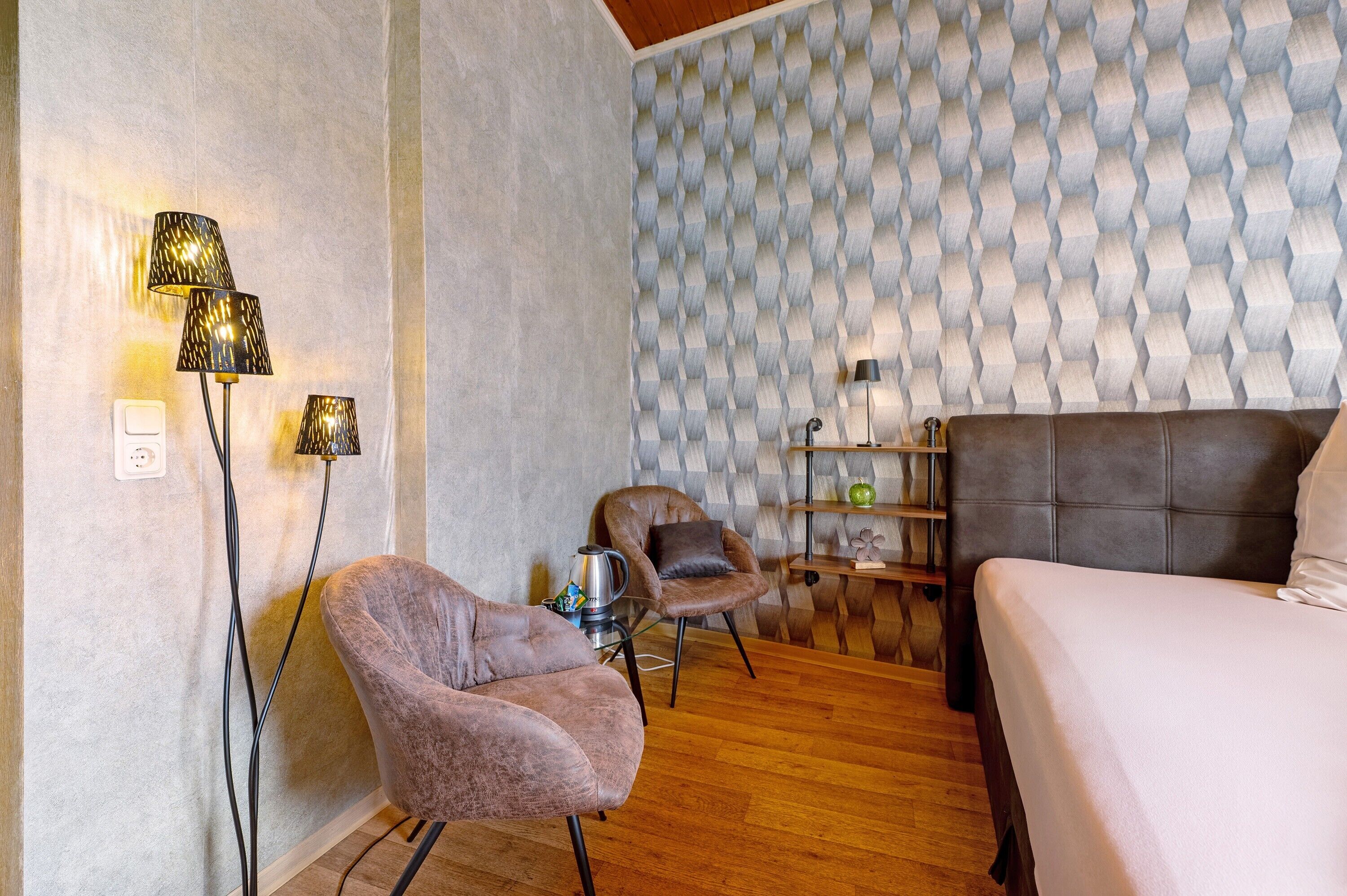 Une pièce comprenant un lit, deux chaises, une table et un mur orné d’un motif texturé.
