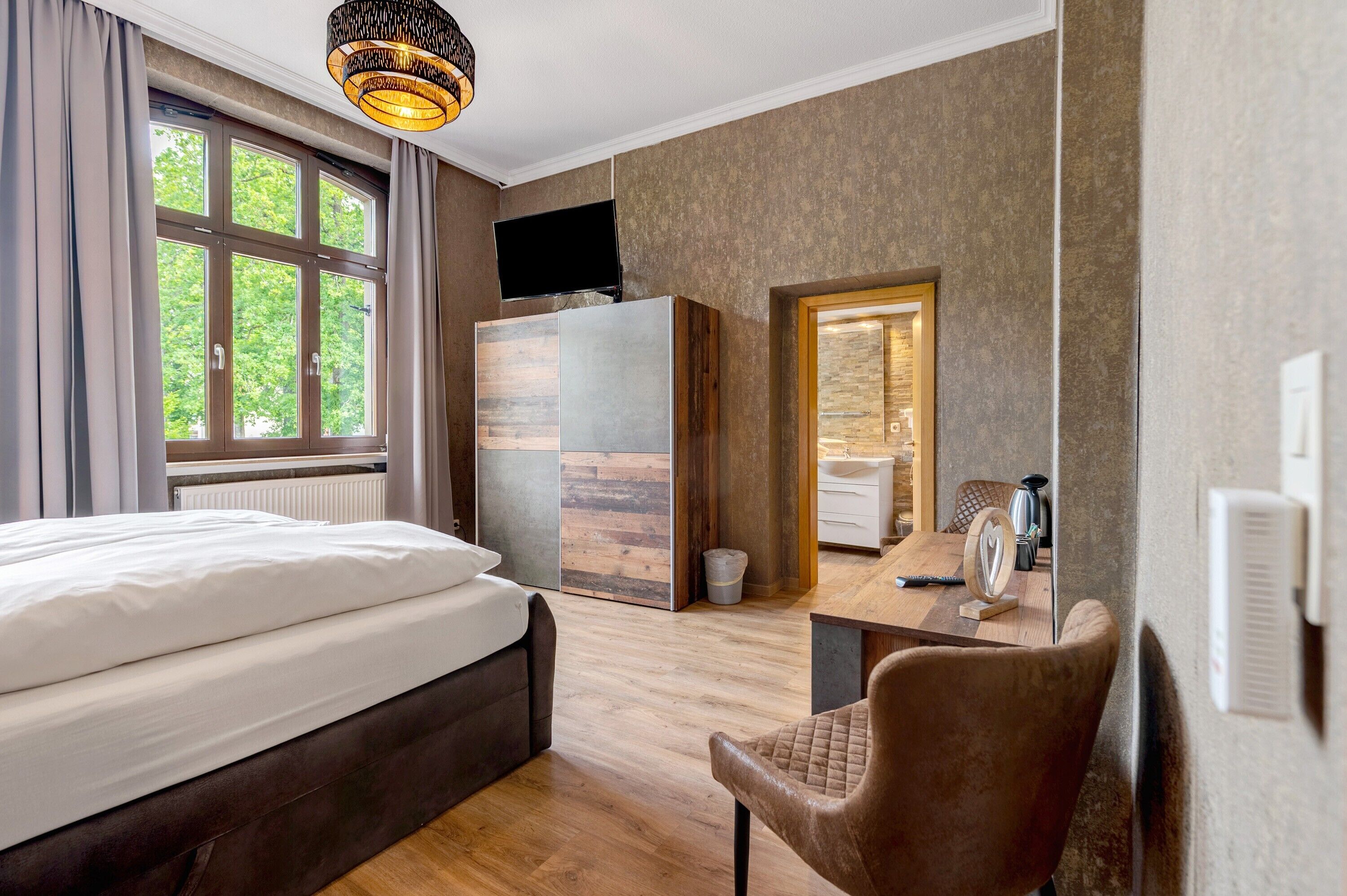 A hotel room with a bed, a desk, a chair, a television, and a window with curtains.