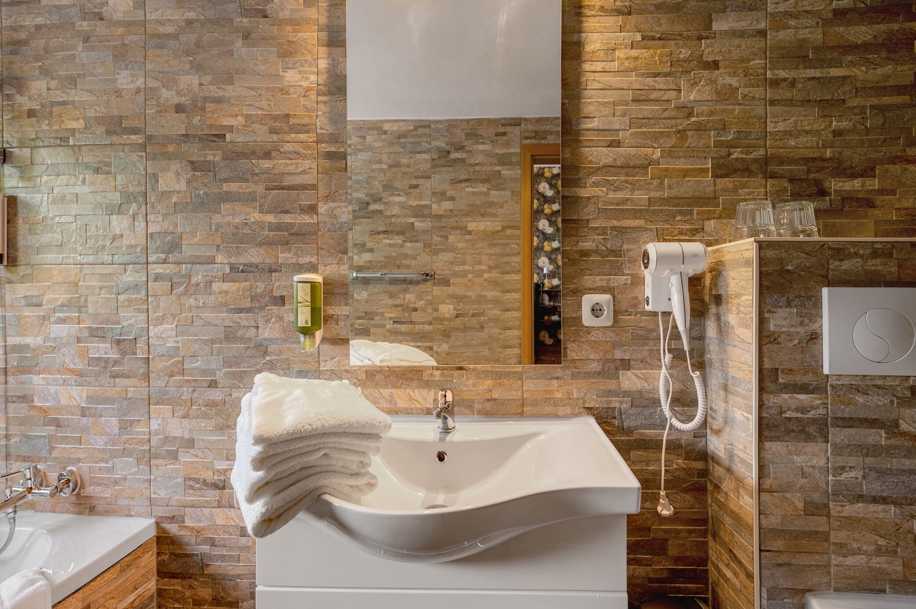 Une salle de bain avec un mur en pierre, un lavabo, un miroir, un porte-serviettes et un espace douche.