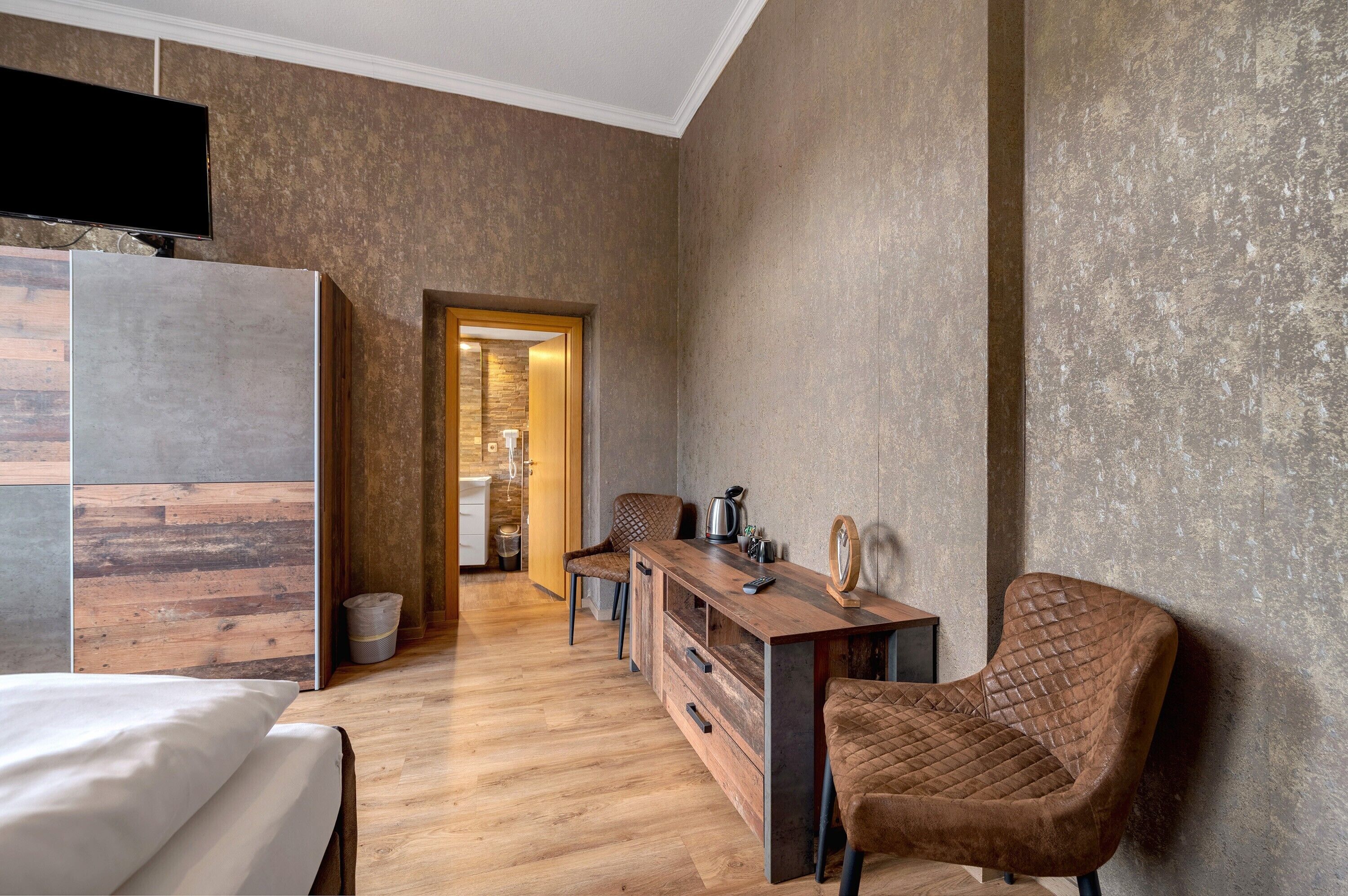 Una moderna camera d'hotel con pavimento in legno, un letto, una scrivania con sedia e un televisore montato a parete.