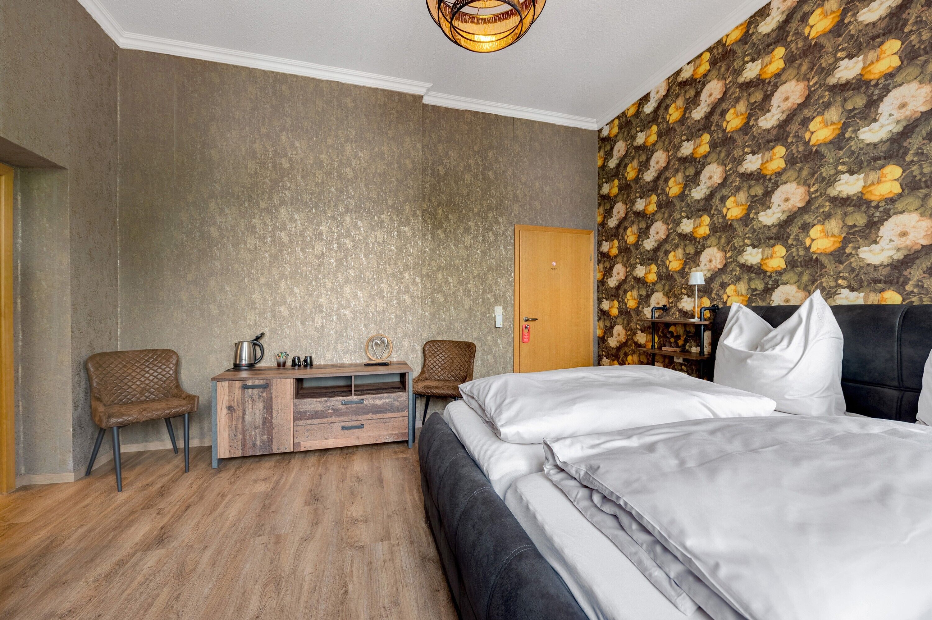 Une chambre à coucher avec un lit, deux chaises, une commode en bois, une table de chevet et une porte.
