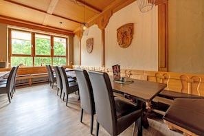 A dining area with wooden tables and chairs, large windows with blinds, and decorative wall art.