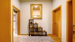 Un pasillo con suelo de madera, alfombra blanca, estantería de madera y un espejo en la pared.