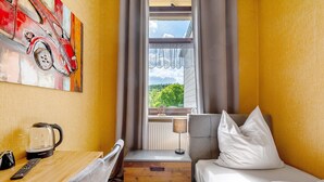 Habitación de hotel con cama, escritorio con hervidor, lámpara y un cuadro de un coche.