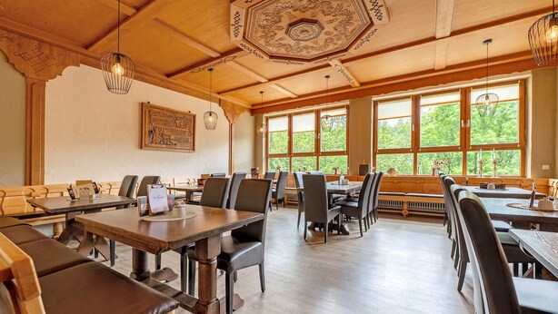 A restaurant with wooden tables and chairs, large windows with a view of greenery, and a decorative ceiling. - Room 'Zimmer 4' with Wi-Fi (Prüm)