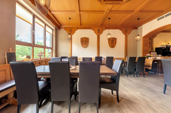 Un comedor con mesas y sillas de madera, ventanas amplias y escudos decorativos en las paredes.