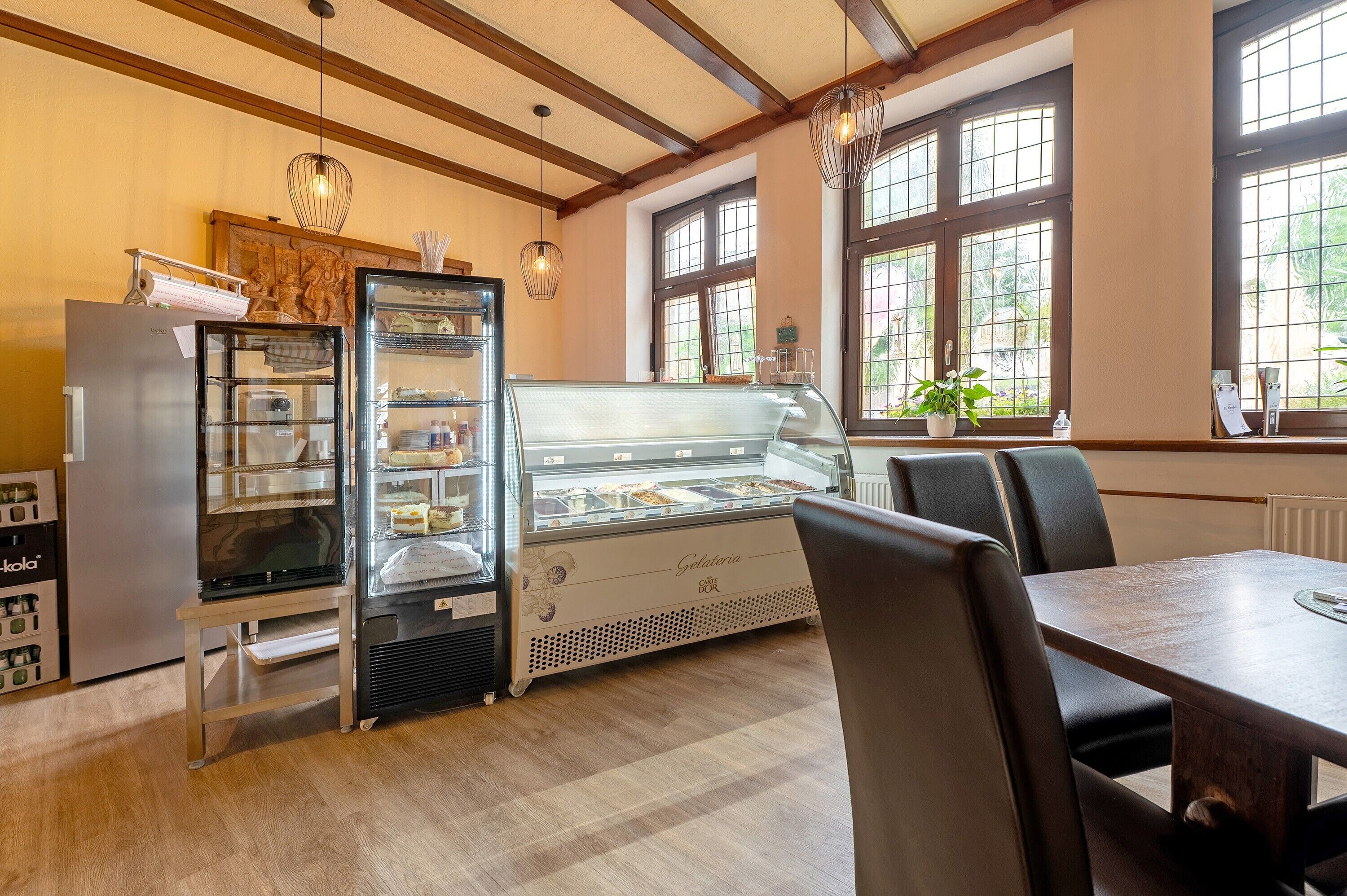 A restaurant interior with a dessert display case, a refrigerator, and a dining table with chairs.