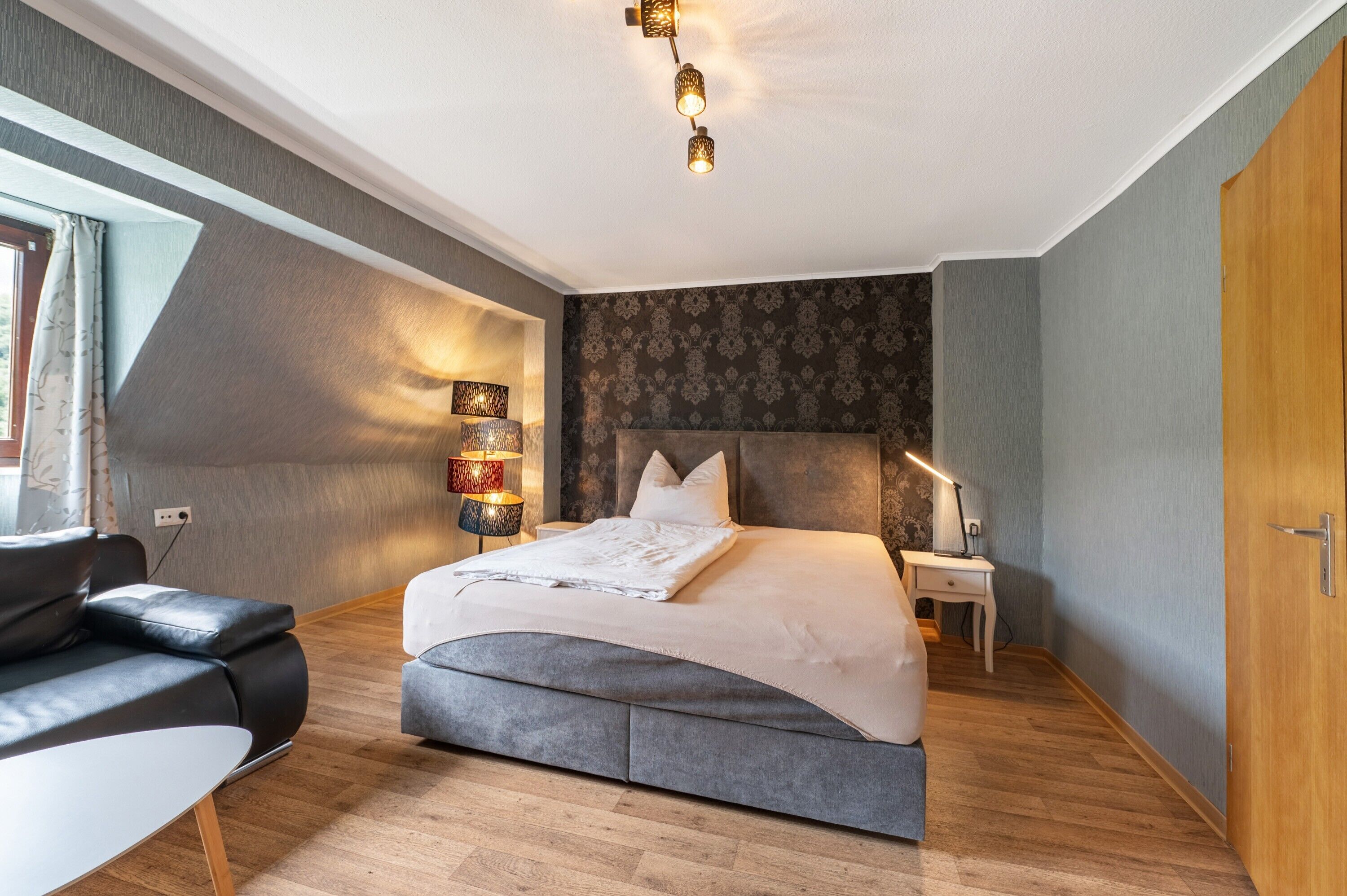 A modern bedroom with a bed, bedside table, lamp, and a view of the outdoors.