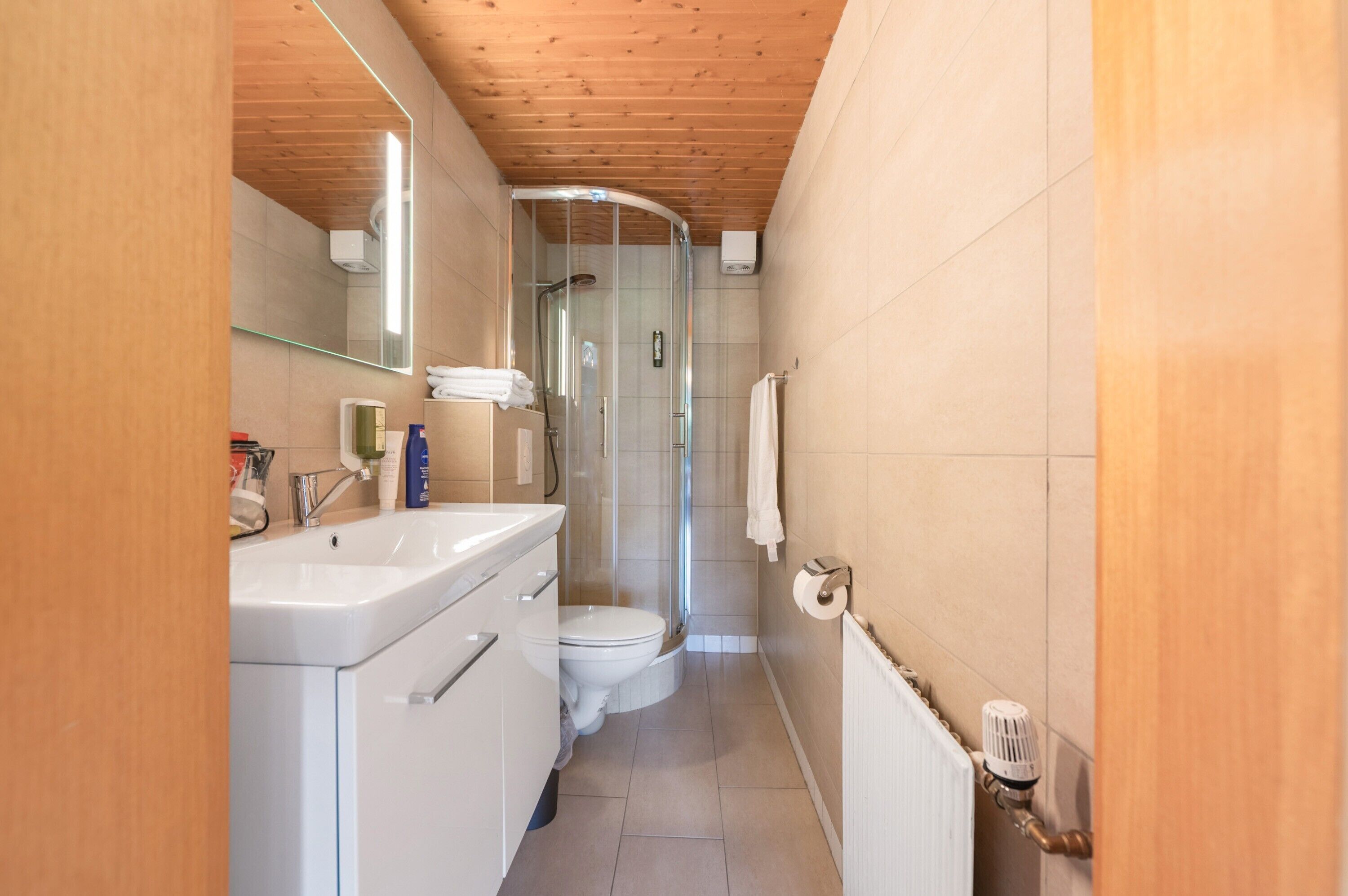 Ein schmales Badezimmer mit Dusche, Toilette und Waschbecken.
