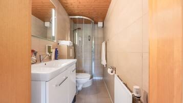 Ein schmales Badezimmer mit Dusche, Toilette und Waschbecken.