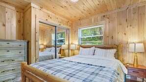 Quarto com painéis de madeira, cama, cômoda e janela.