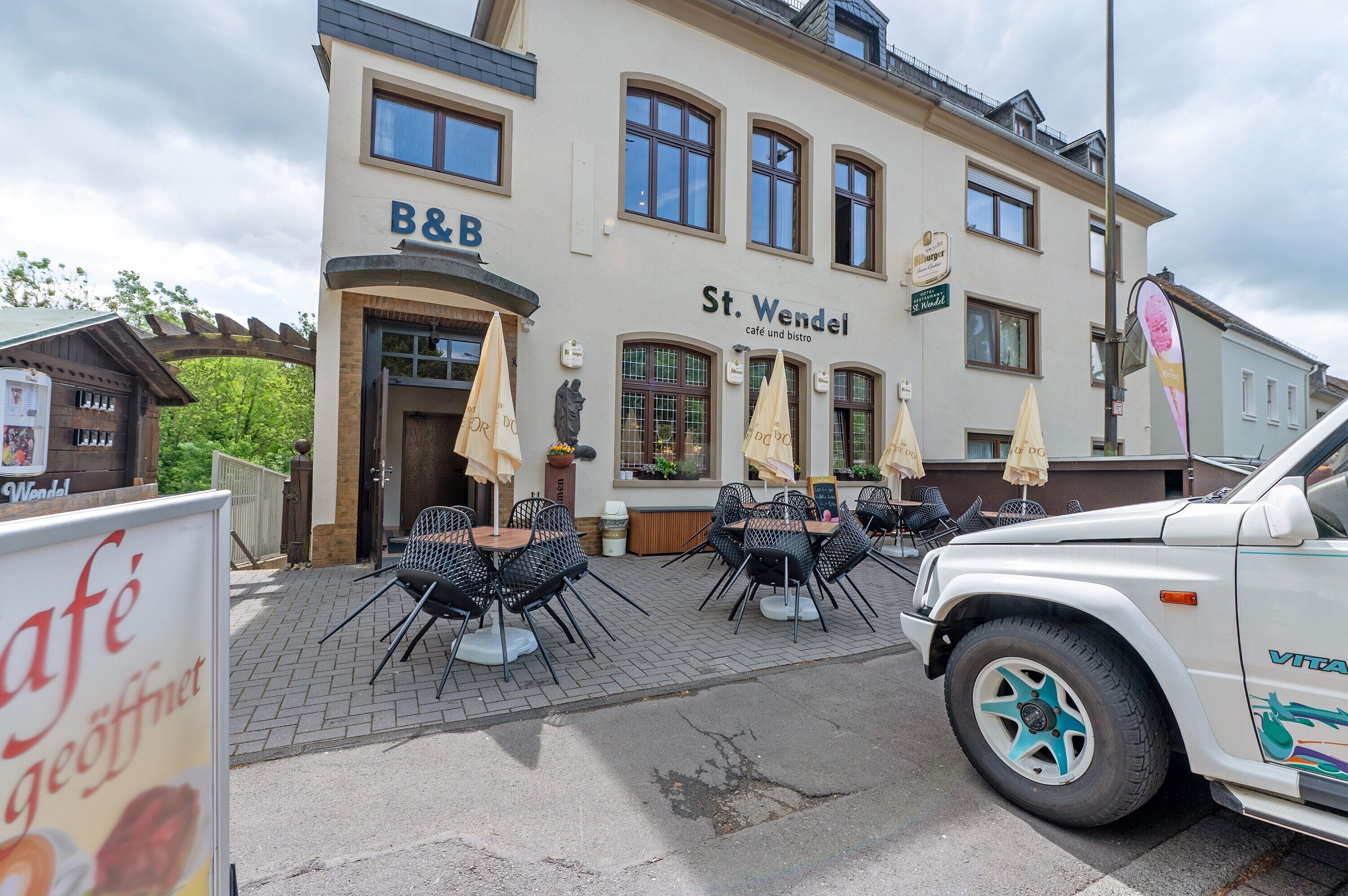A building with a sign reading 'B&B St. Wendel' and outdoor seating with umbrellas.