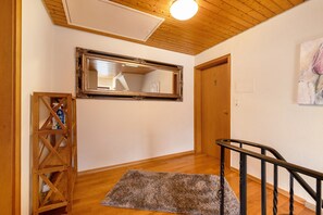 Un couloir doté d’un plancher en bois, d’un miroir, d’une porte en bois et d’un escalier avec une rampe noire.