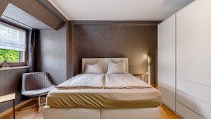 Un llit ben arriscat en una habitació amb finestra, una cadira i una taula de nit.