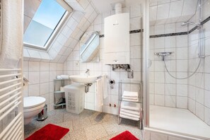 Un baño moderno con tragaluz, ducha, inodoro y lavamanos.
