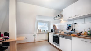 Une cuisine moderne avec des meubles blancs, un four encastré, un four à micro-ondes et une fenêtre avec des stores.
