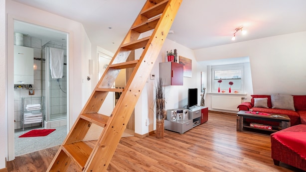 Un espace de vie moderne avec un escalier en bois, un canapé rouge, un téléviseur et un coin cuisine.