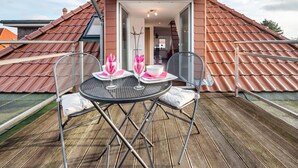 Une terrasse sur le toit avec une table et des chaises, une petite table ornée d’un vase et d’un bol, et une vue sur l’immeuble voisin.