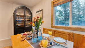 A breakfast table set with various food items, a vase with flowers, and a window with a view of trees.