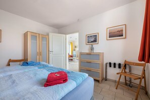 Un dormitorio con cama, armario, silla, radiador y un cuadro en la pared.