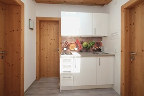 A compact kitchen with wooden doors, white cabinets, and a backsplash with fruit and vegetables. - Apartment 'Appartement Gletscherblick' with Mountain View, Private Terrace and Wi-Fi (Medraz)