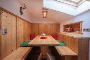 A wooden-paneled room with a central table, benches, a skylight, and a wall-mounted shelf with decorative items. - Apartment 'Appartement Gletscherblick' with Mountain View, Private Terrace and Wi-Fi (Medraz)