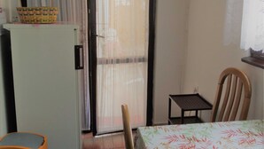 Une petite pièce comprenant un lit, une table, une chaise, un réfrigérateur et une fenêtre avec un rideau.