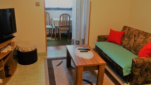 Un salon avec une télévision, un canapé, une petite table et une vue sur le balcon.