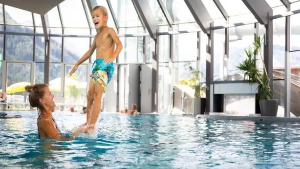 A swimming pool with a glass ceiling, indoor plants, and a view of the outdoors.