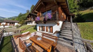 A chalet with a wooden balcony, outdoor seating, and a view of the surrounding landscape.