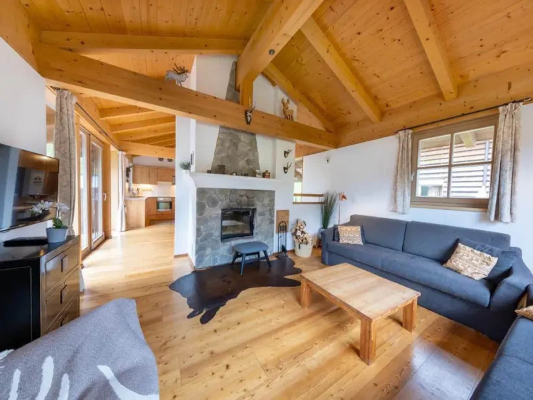 A spacious living area with a fireplace, wooden beams, a sofa, and a dining area.