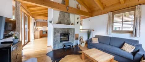 A spacious living area with a fireplace, wooden beams, a sofa, and a dining area.
