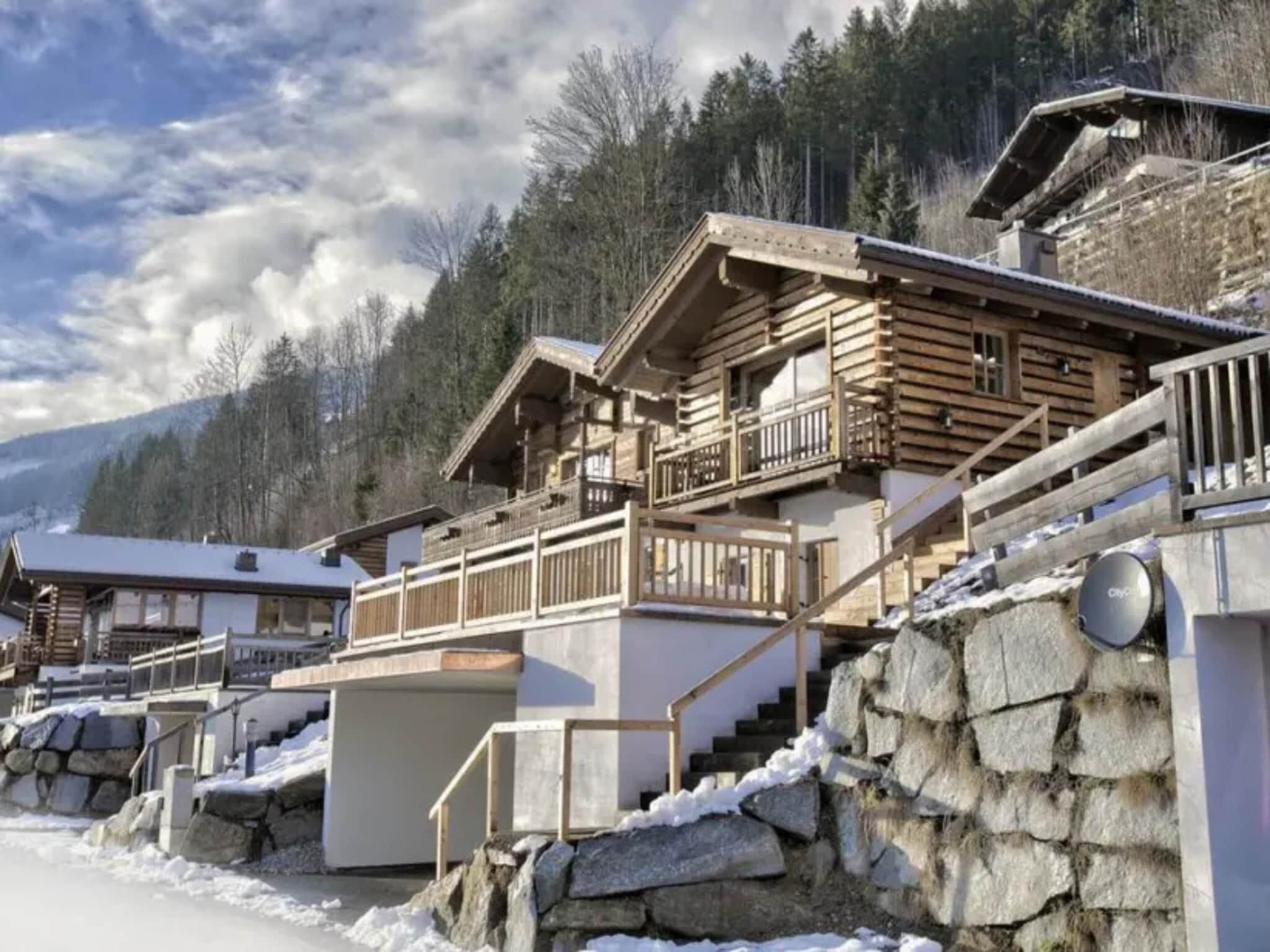 A wooden cabin with a balcony, stone steps, and a mountain backdrop.
