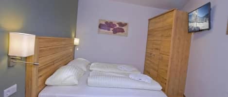 A single bed with a wooden frame, a bedside table, a wall-mounted lamp, and a painting on the wall.