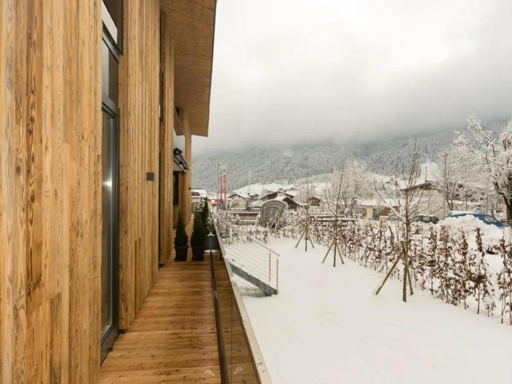 Un balcon en bois offrant une vue sur un paysage enneigé et des bâtiments.
