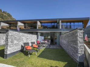 Une maison moderne à deux étages, dotée d’une façade en pierre, d’un toit plat et d’une véranda en verre.