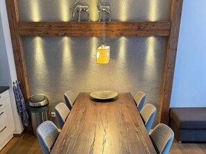 Ein Essbereich mit einem Holztisch, sechs Stühlen, einer kleinen Mülltonne und einer Pendelleuchte.
