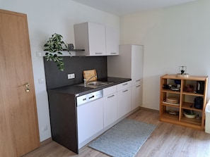Cocina compacta con lavavajillas, un lavabo y un estante de madera con utensilios de cocina.