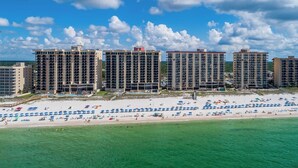 A beachfront hotel with multiple high-rise buildings, a sandy beach with umbrellas, and a clear blue sky. - Phoenix IV 4142 (Orange Beach)