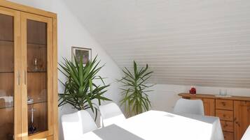 A dining area with a table, chairs, a wooden cabinet, and potted plants.