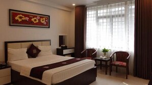 Une chambre d’hôtel avec un grand lit, un bureau, une chaise, une fenêtre avec des rideaux et un tableau au mur.