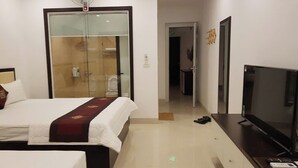 Une chambre d’hôtel comprenant un lit, une télévision, une porte vitrée donnant accès à la salle de bain et un couloir.