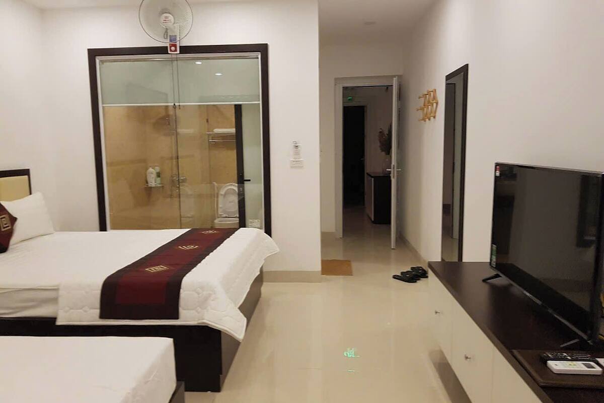 A hotel room with a bed, a TV, a glass door leading to a bathroom, and a hallway.