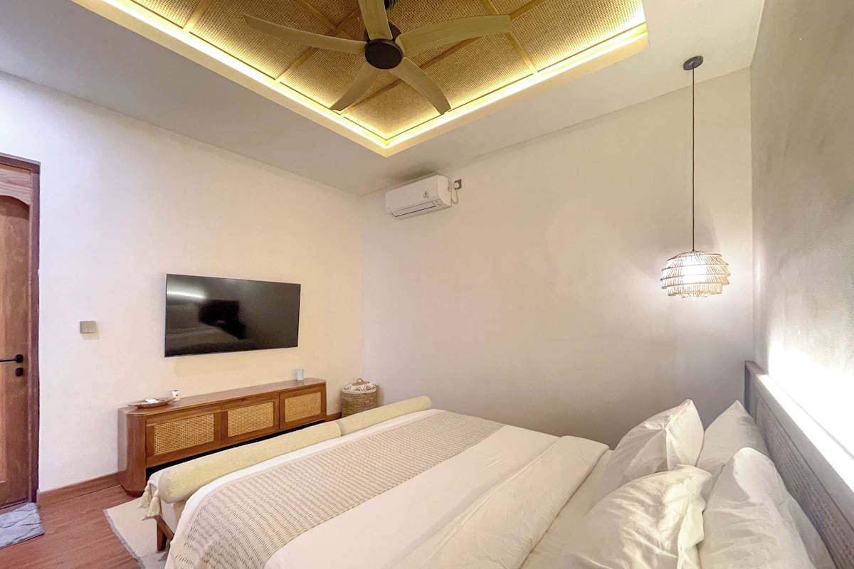 A bedroom with a bed, a television, a ceiling fan, and a hanging light fixture.