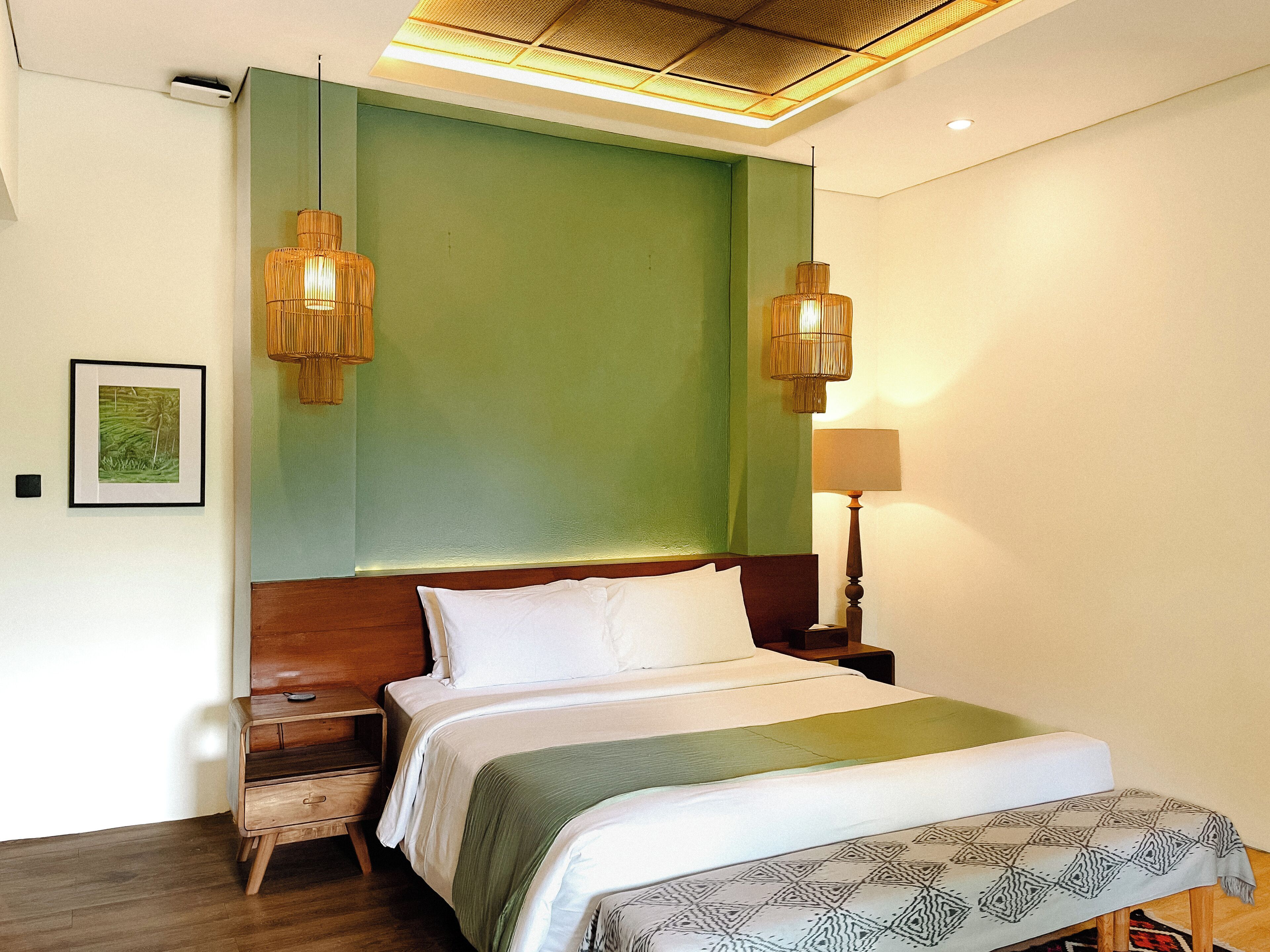 Quarto de hotel com uma cama, mesas de cabeceira, abajur e um quadro na parede.