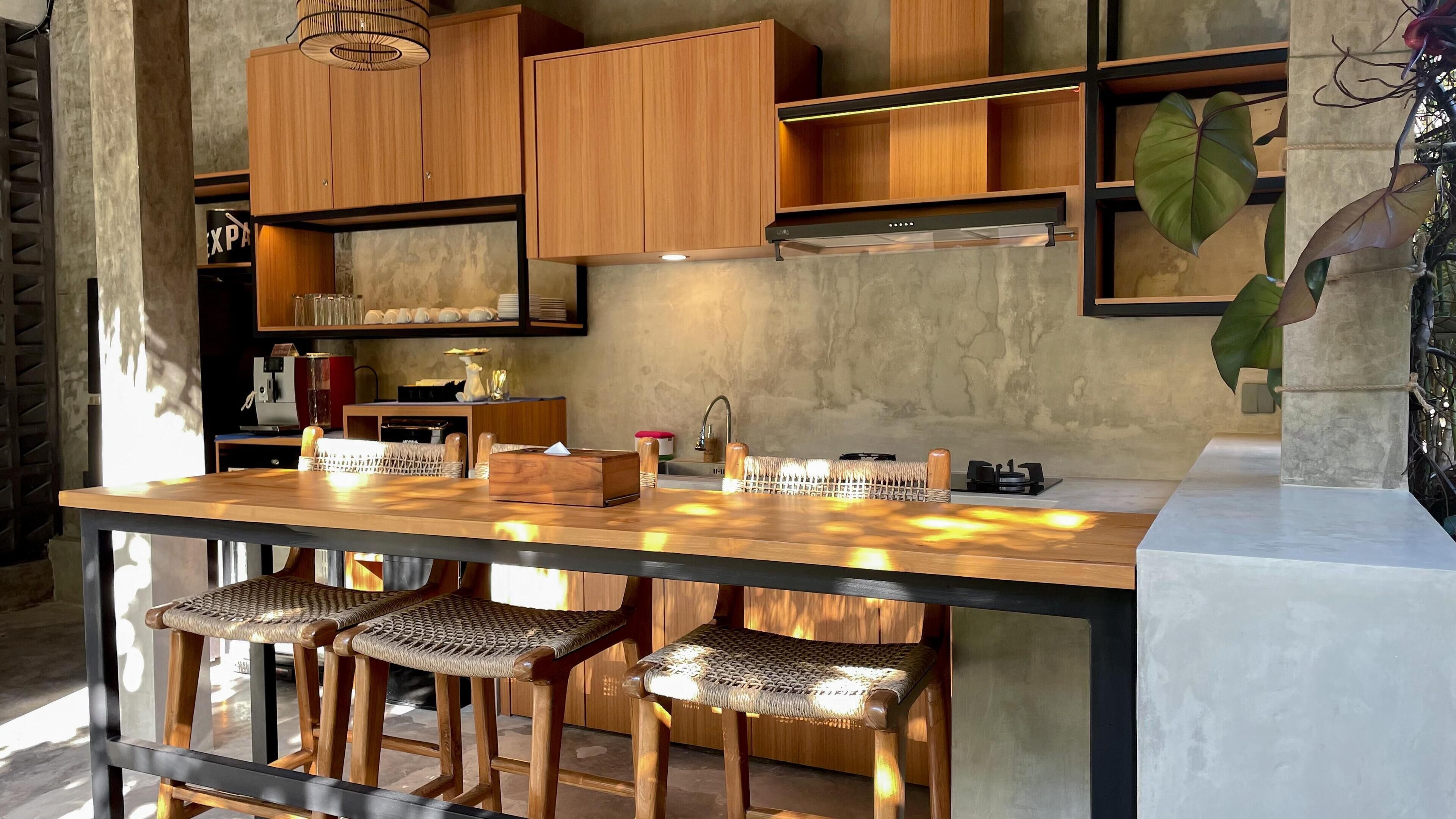 A modern kitchen with wooden cabinets, a bar area with stools, and a large plant.