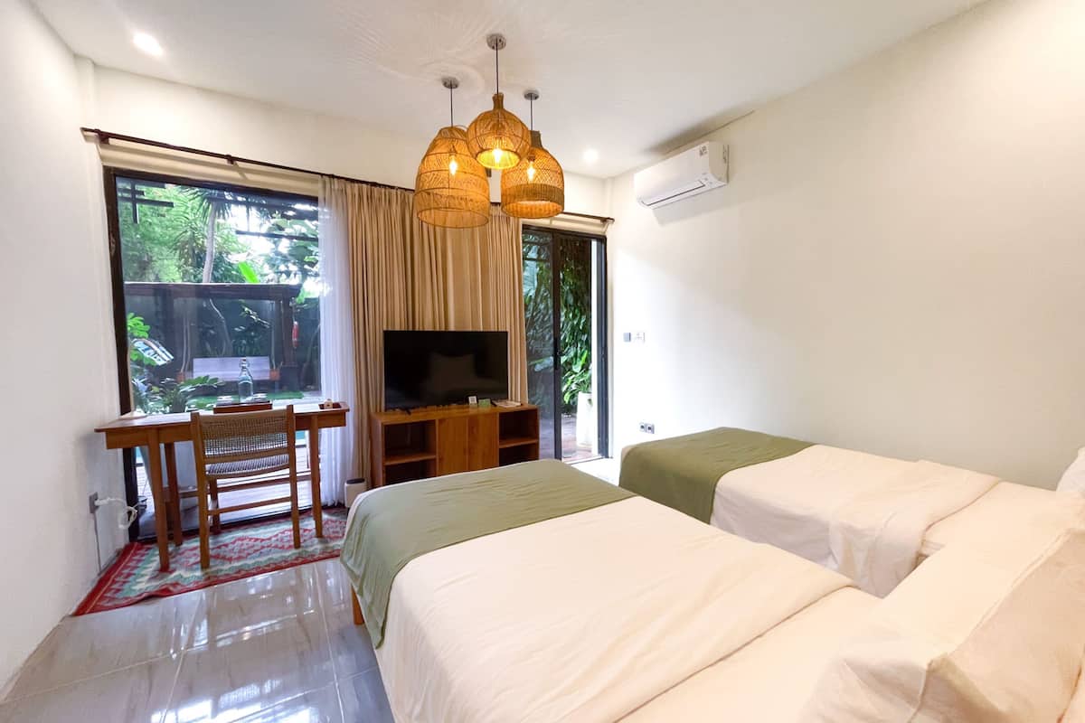 A bedroom with two beds, a TV, a desk, and a window with curtains.