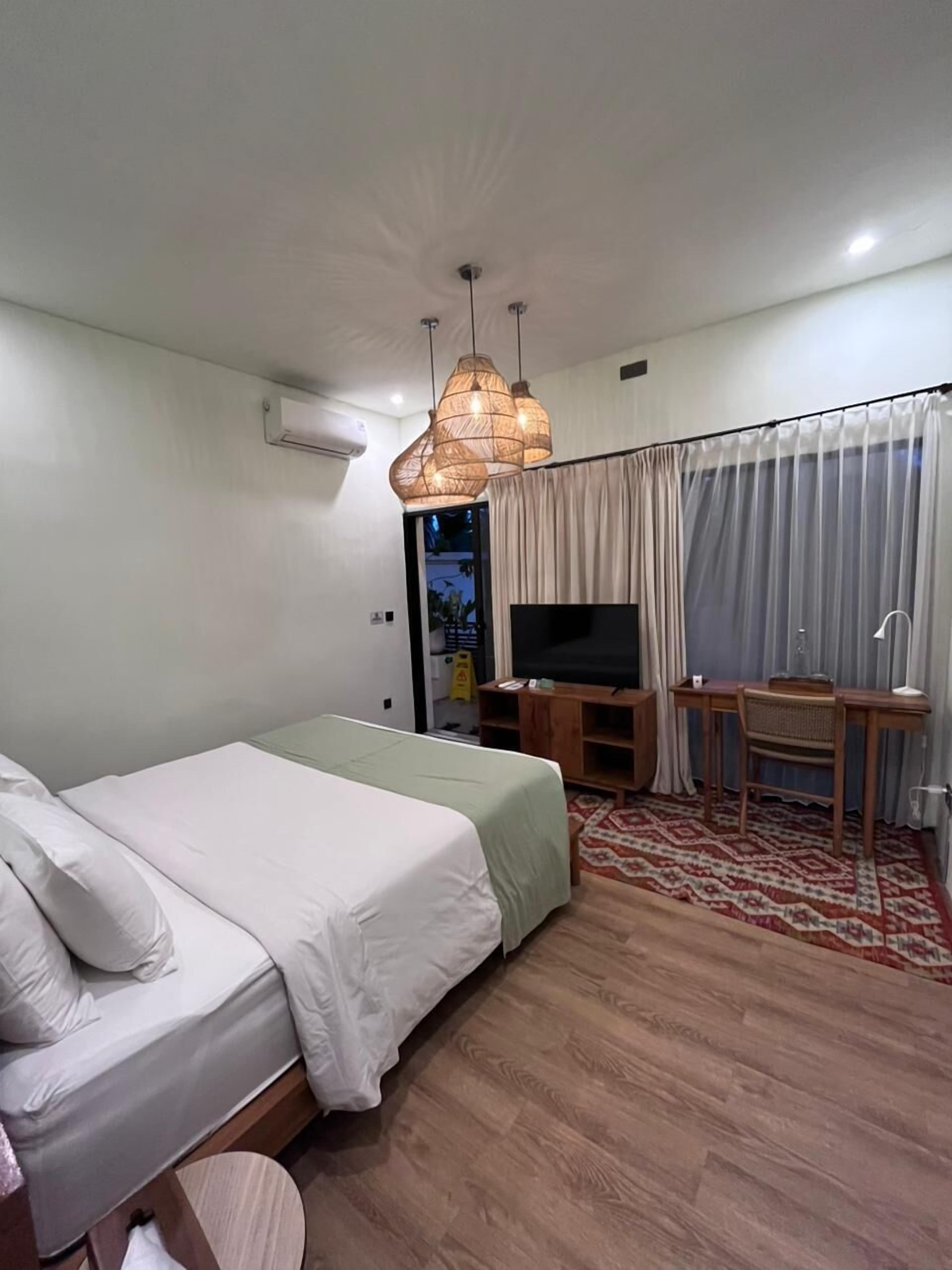 A hotel room with a bed, a desk with a chair, a television, and a window with curtains.
