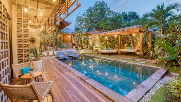 A pool area with wooden deck, lounge chairs, and a pergola with string lights. - Leafy Home Canggu (Canggu)